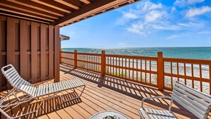 A wooden deck with two lounge chairs and a table, overlooking a beach with a wooden railing. - Gulf Front Escape on the Beach with Shared Viewing Deck & Pool - Cozy & Intimate (Englewood)