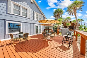 A wooden deck with outdoor furniture, a large umbrella, and palm trees. - Gulf Front Escape on the Beach with Shared Viewing Deck & Pool - Cozy & Intimate (Englewood)
