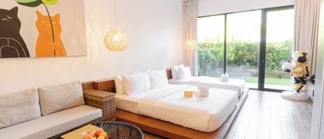 A modern hotel room with a sofa, a bed, a wicker coffee table with fruit, and a large window with a view.