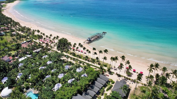 Un resort en la playa con palmeras, una piscina y vista al océano.