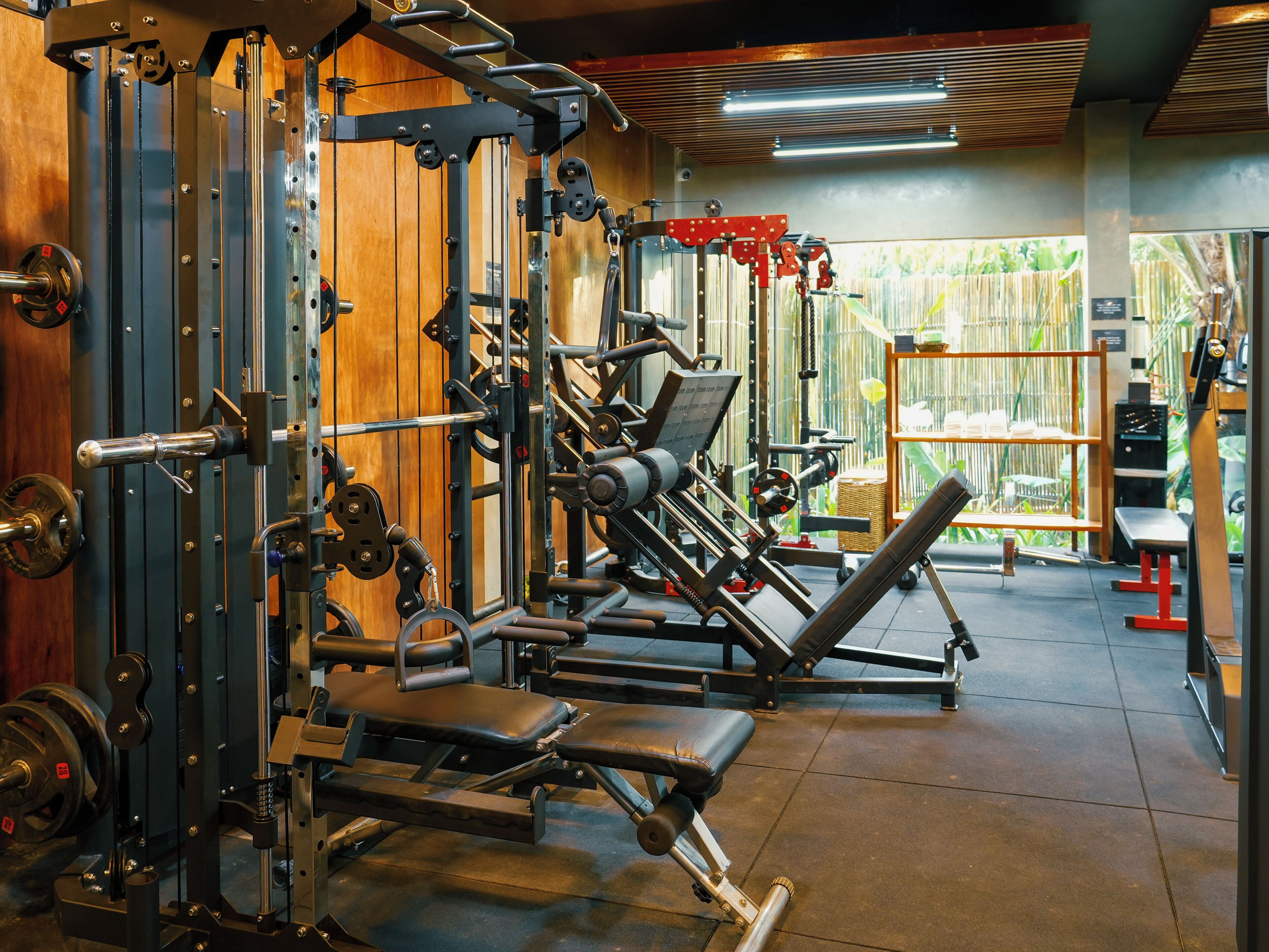 A gym with various exercise machines, a bench, and a wall with a wooden panel.