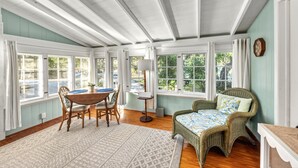 A sunroom with a dining table, chairs, wicker furniture, and large windows.