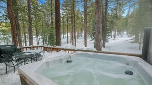 Un bain à remous installé dans une forêt enneigée, avec une table et des chaises à proximité.