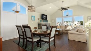 A spacious living area with a dining table, chairs, a sofa, and a ceiling fan. - Rhapsody in Blue: Oceanside, Hot Tub, Foosball Table, Community Amenities (Corolla)