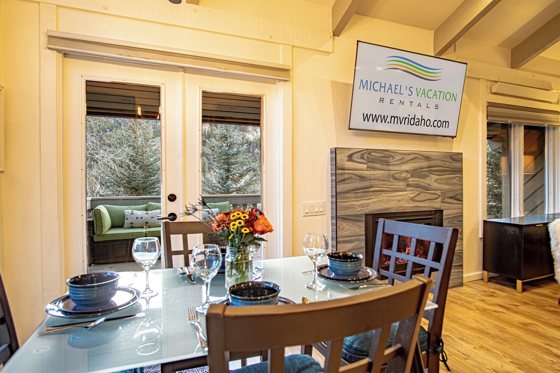 A dining area with a glass table set for four, a fireplace, and a sign for Michael's Vacation Rentals.