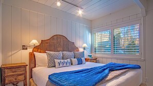 Ein Schlafzimmer mit einem hölzernen Kopfteil, einem großen Bett mit vielen Kissen, zwei Nachttischen und einem Fenster mit Jalousien.