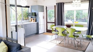 A modern kitchen with a refrigerator, microwave, and a dining area with green chairs and a table. - Kiwi Bach with Amazing Views (Wānaka)