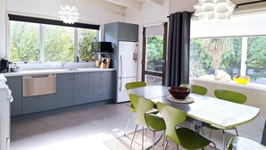 A modern kitchen with grey cabinets, a white countertop, and a dining area with green chairs. - Kiwi Bach with Amazing Views (Wānaka)