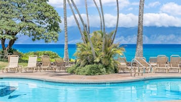 A pool with lounge chairs and palm trees, overlooking a clear blue ocean.