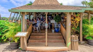 A covered outdoor seating area with a tiled roof, surrounded by potted plants and a sign indicating a waiting area. - Studio Relaxing Garden View Retreat Near Napili Bay & Ocean-Napili Shores D230 (Lahaina)