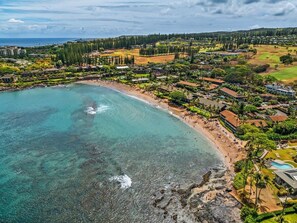 Luftaufnahme eines Küstenresorts mit Strand, klarem Wasser und einer Mischung aus Wohn- und Hotelgebäuden.