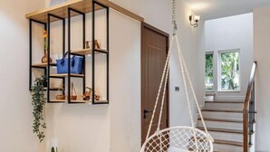 A modern interior with a wooden staircase, a white hanging chair, and a black metal shelf unit with decorative items. - 3 bedroom Villa Venus House Phan Thiet (Phan Thiet)
