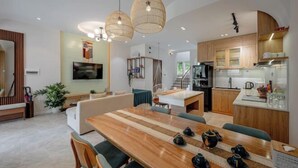 A modern kitchen with wooden cabinets, a dining area with a wooden table, and a living room with a sofa and a TV. - 3 bedroom Villa Venus House Phan Thiet (Phan Thiet)