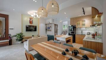 A modern kitchen with wooden cabinets, a dining area with a wooden table and chairs, and a living area with a sofa and a TV.