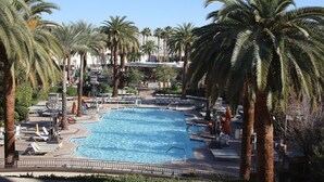 Ein Swimmingpool, umgeben von Palmen, mit Liegestühlen und Sonnenschirmen.