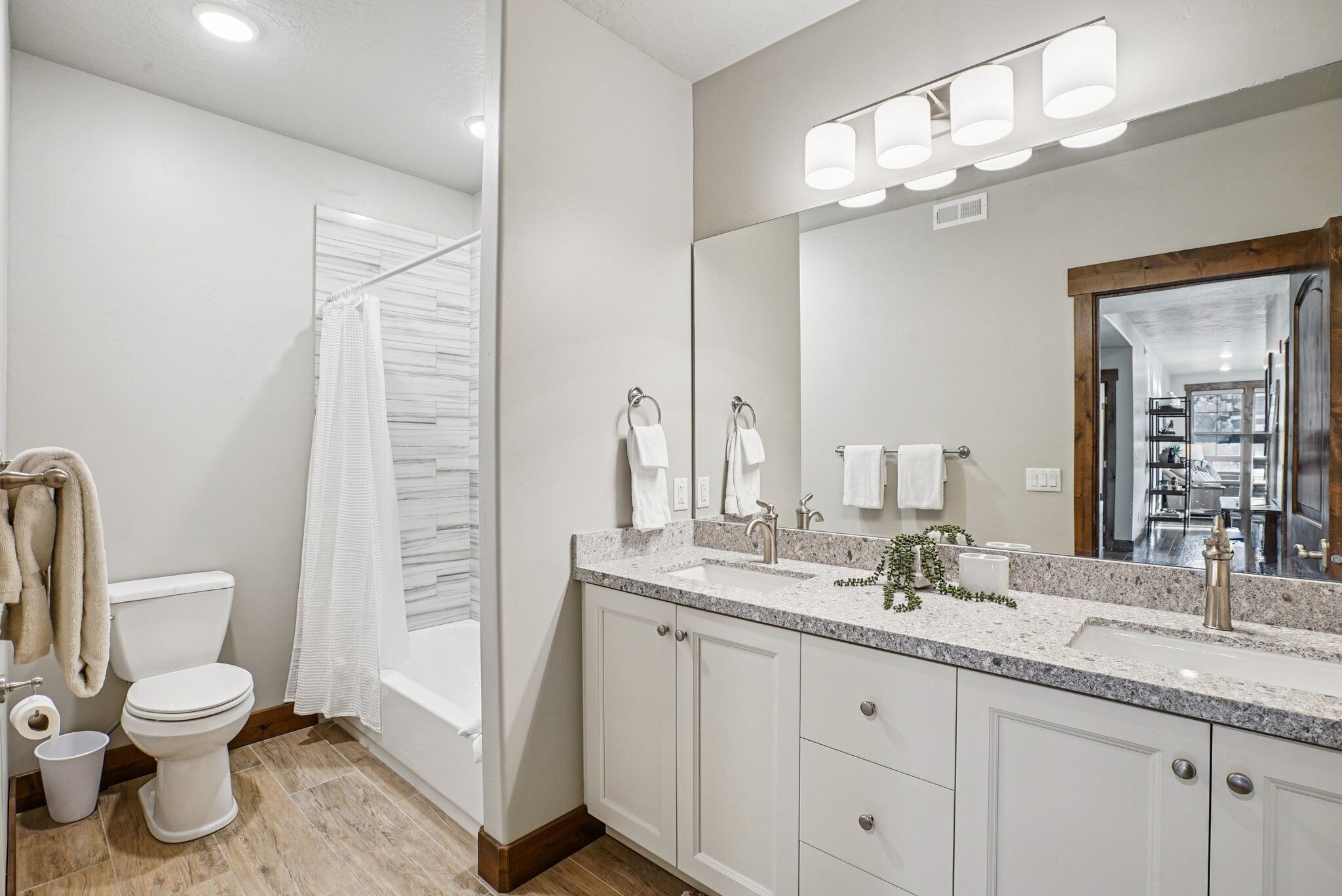 A modern bathroom with a white toilet, a shower with a curtain, a sink with a mirror, and a countertop with a plant.