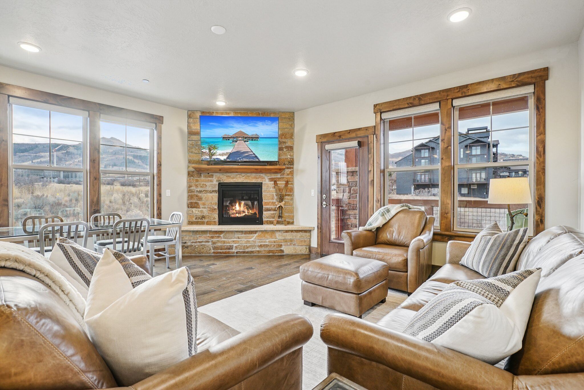 A spacious living room with a stone fireplace, leather sofas, and large windows offering a view of the mountains.