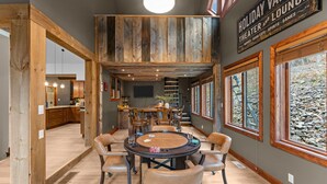 A spacious room with a wooden ceiling, a round table with chairs, and large windows with a view of rocks.