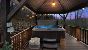 A wooden deck with a hot tub, outdoor seating, and string lights.