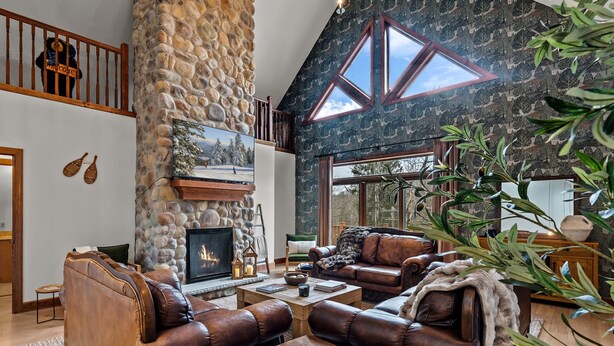 A cozy living room with leather sofas, a stone fireplace, and a large window.