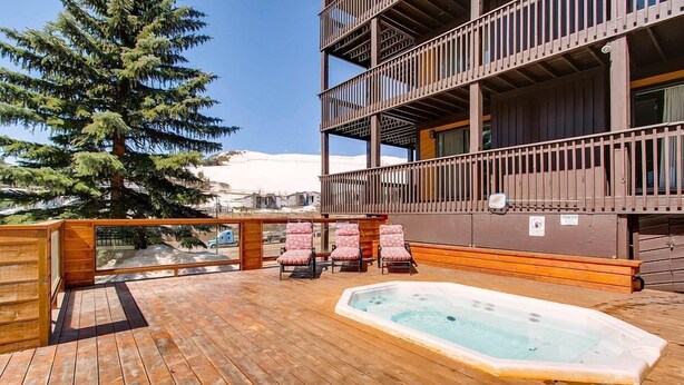 Eine Holzterrasse mit Whirlpool, Liegestühlen und Blick auf einen Berg.