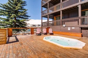 Una terraza de madera con un jacuzzi, sillas de descanso y vistas a una montaña.