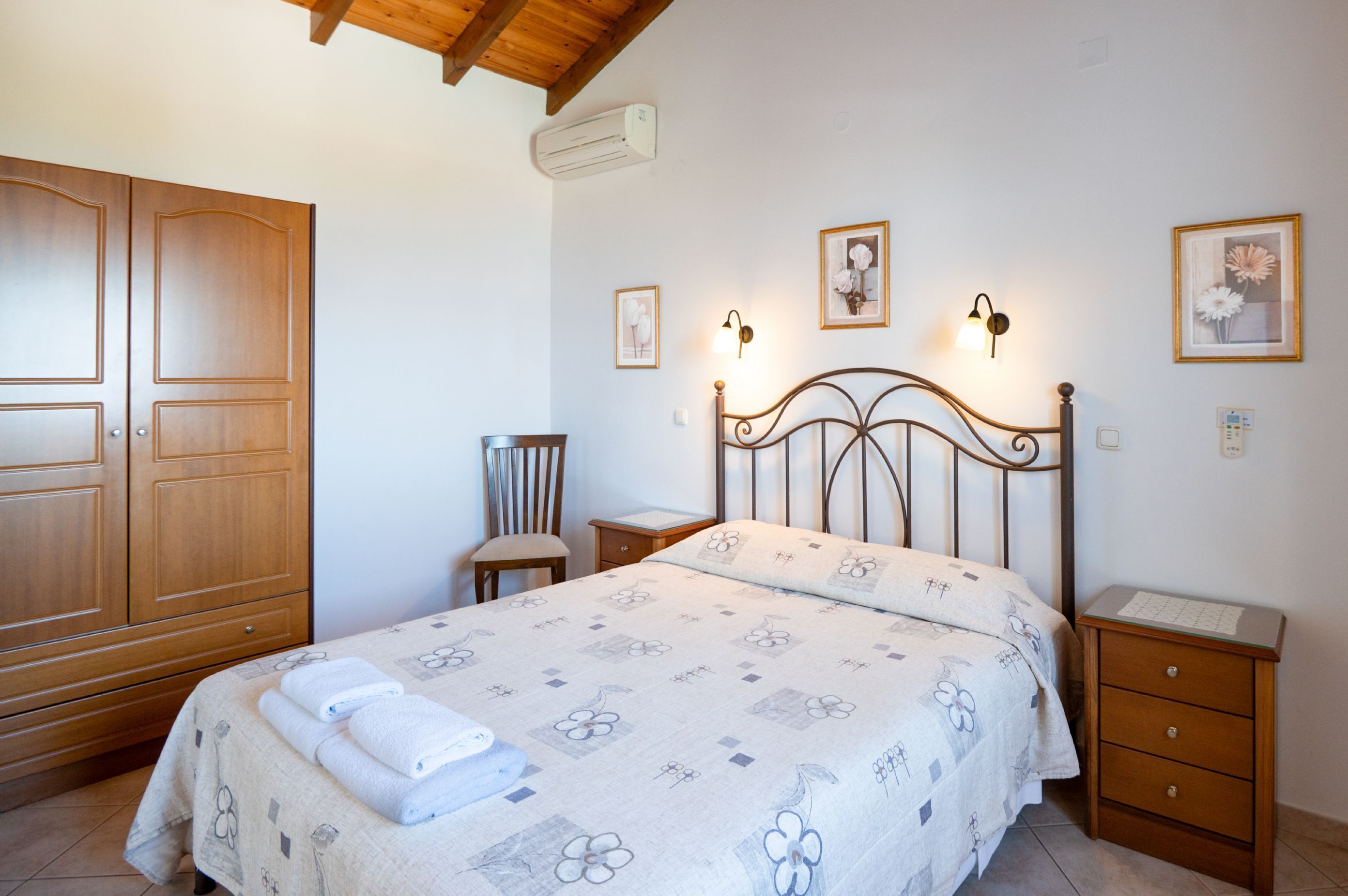 A bedroom with a bed, wooden wardrobe, two bedside tables, a chair, and wall-mounted lights.
