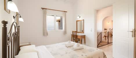 A hotel room with a bed, a desk, a chair, a window with curtains, a mirror, and a door leading to another room.