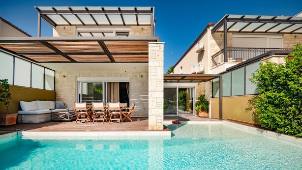 Un espace piscine extérieur moderne doté d’une terrasse ensoleillée, de sièges et offrant une vue dégagée sur la piscine.