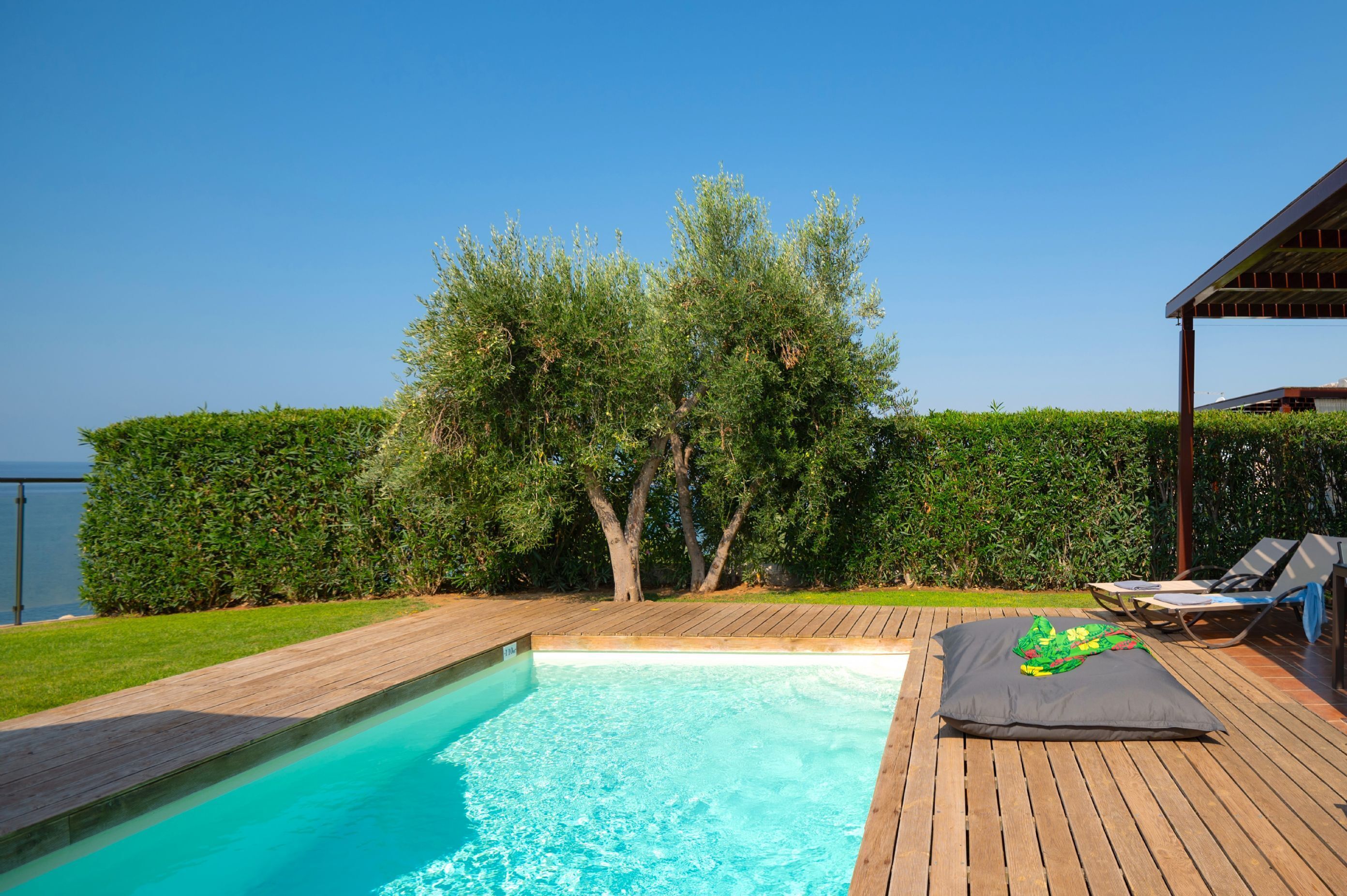A swimming pool with a wooden deck, a lounge area with sun loungers, and a view of the sea.
