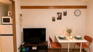 A compact living space with a TV, dining table, chairs, a microwave, and a refrigerator. - YMK Oshiage 7A (Tokyo)