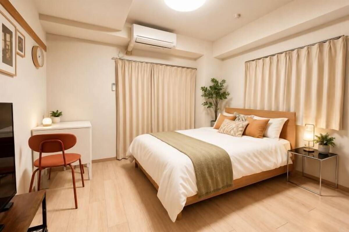 A bedroom with a bed, a desk, a chair, an air conditioner, and curtains.