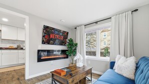 Moderni olohuone, jossa on sininen sohva, puinen sohvapöytä, takka ja suuri Netflix-juliste seinällä.