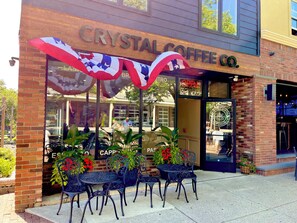Un edificio de ladrillo con un letrero que dice 'Crystal Coffee Co.' y mesas y sillas de metal para disfrutar al aire libre.