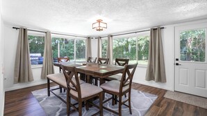 A dining area with a wooden table and chairs, large windows with curtains, and a ceiling light fixture. - Crystal River Getaway (Crystal River)