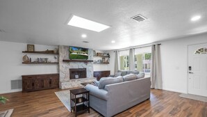 A spacious living room with a stone fireplace, a grey sofa, wooden flooring, and a large window with curtains. - Crystal River Getaway (Crystal River)