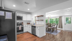 A modern kitchen with white cabinets, stainless steel appliances, and a wooden dining area with a table and chairs. - Crystal River Getaway (Crystal River)