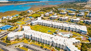 Vista aérea de un complejo residencial con varios edificios de apartamentos, un espacio verde central y una playa cercana.