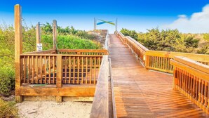 Un muelle de madera que conduce a una zona de playa, con un cartel que indica un área de estacionamiento.