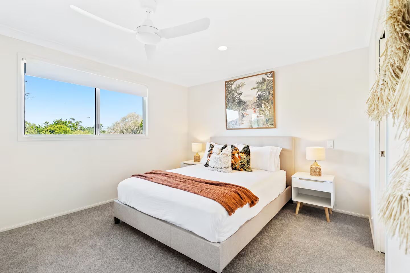 A bedroom with a bed, two bedside tables, a ceiling fan, a window, and a painting on the wall.