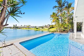 A swimming pool with a clear view of a residential area, including houses and a golf course in the background. - Stunning Waterfront Home - 3 Large Ensuites! (Broadbeach Waters)