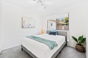 A bedroom with a bed, a bedside table, a lamp, a window with a view, and a plant. - Stunning Waterfront Home - 3 Large Ensuites! (Broadbeach Waters)
