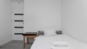 A minimalist hotel room with a bed, a small table, and a door. - Bronowice Spacious Apartment (Kraków)