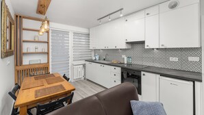 A modern kitchen with white cabinets, a wooden dining table, and a built-in bench. - Bronowice Spacious Apartment (Kraków)