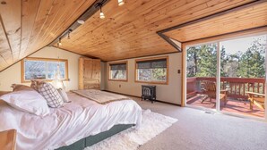 A bedroom with a large bed, a dresser, and a window. There is a balcony with wooden railings and outdoor furniture. - Bear Den|Jacuzzi, AC, Steps from trails, Dogs OK! (Big Bear)