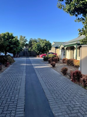 Un chemin pavé mène à une rangée de maisons dotées d’un toit végétalisé, qui sont entourées d’arbres et d’arbustes.