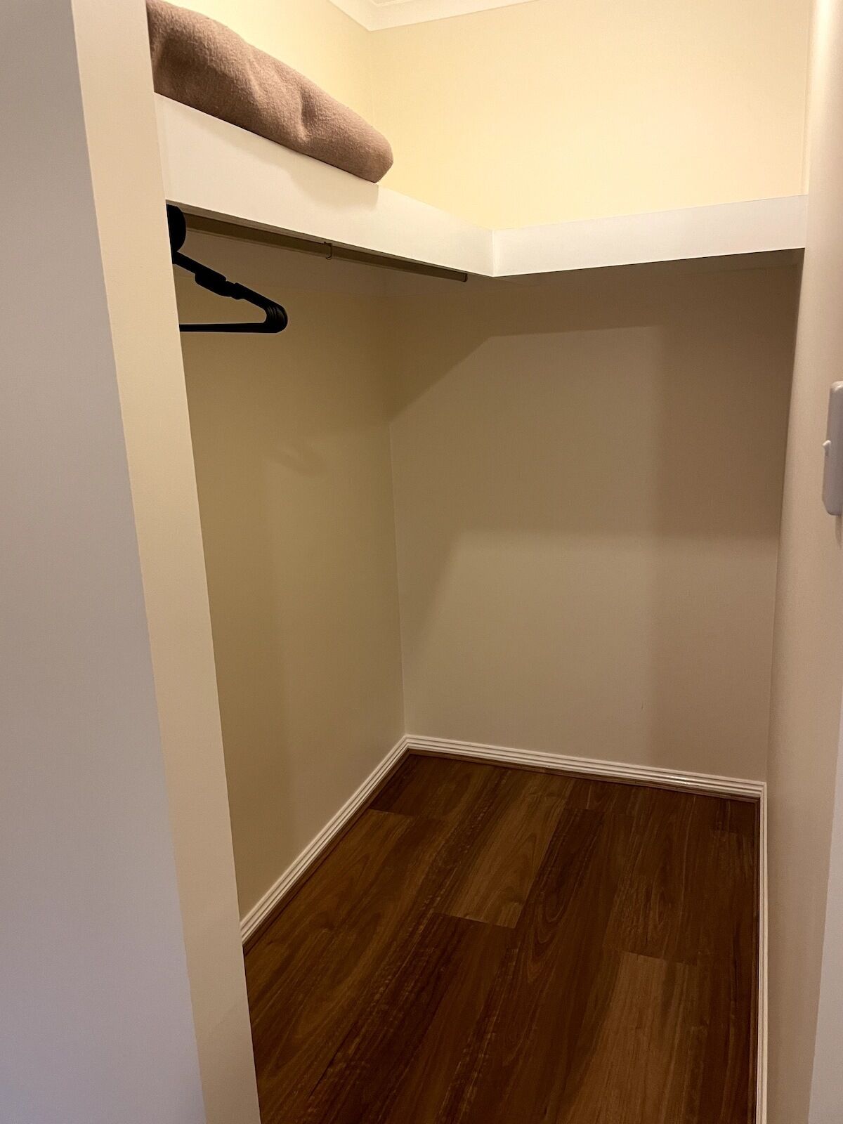 A small, enclosed closet with a wooden floor and a hanging rod.