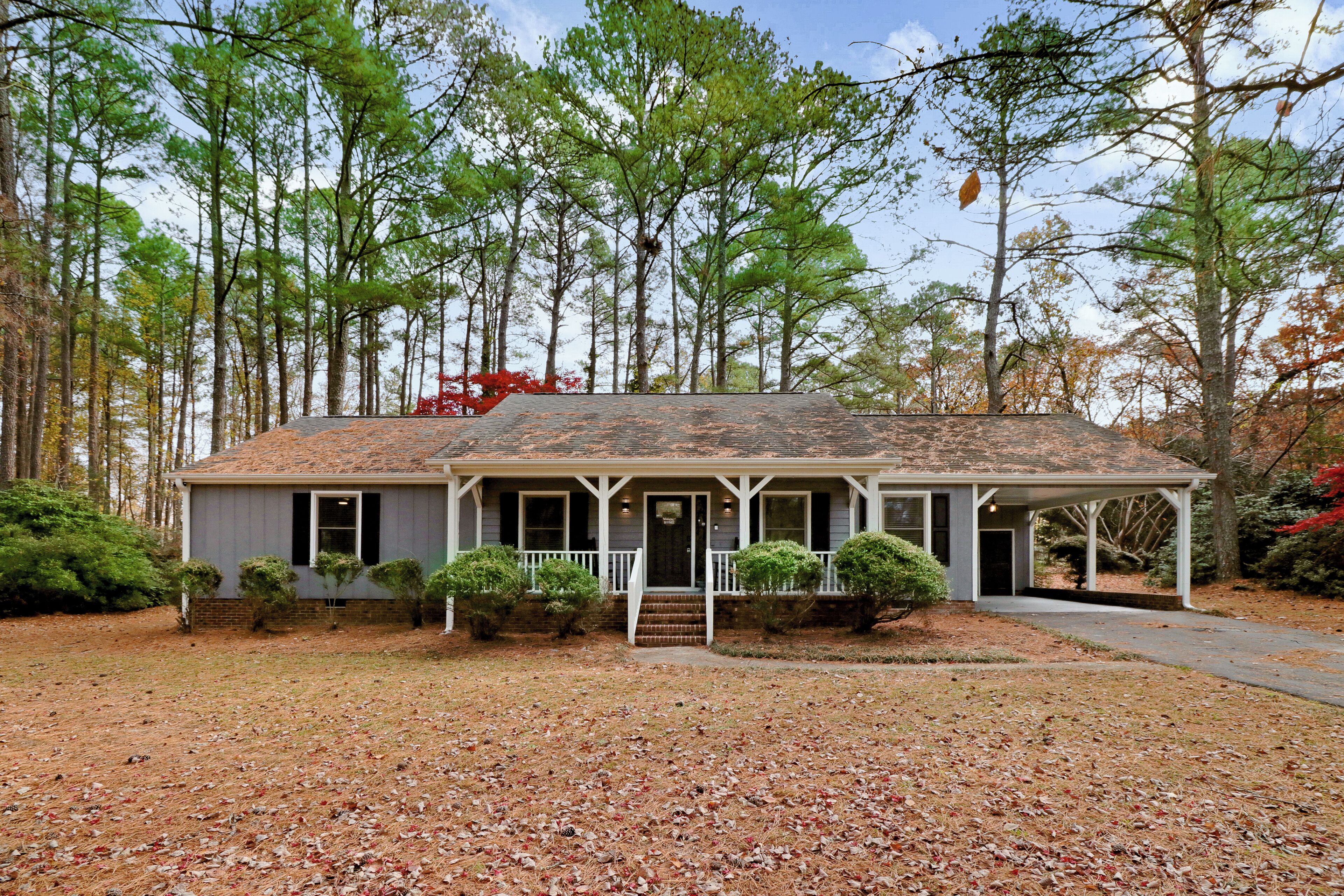 A single-story house with a porch, surrounded by trees and a leaf-covered lawn.