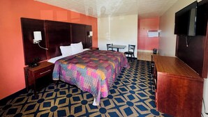 Habitación de hotel con cama, mesita de noche, lámpara, televisor y un escritorio pequeño con sillas.