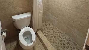 Baño con inodoro, ducha y paredes de azulejos.